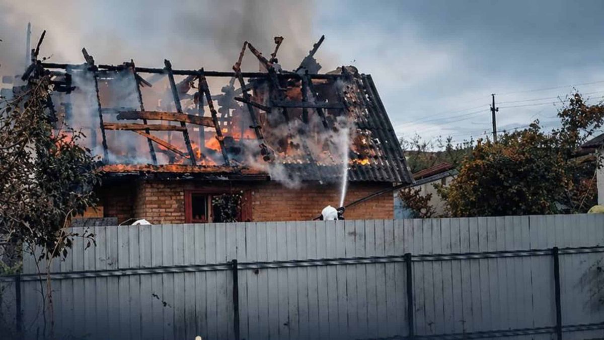 Рятувальник гасить пожежу в приватному будинку зі зруйнованим дахом після атаки РФ на Київщині