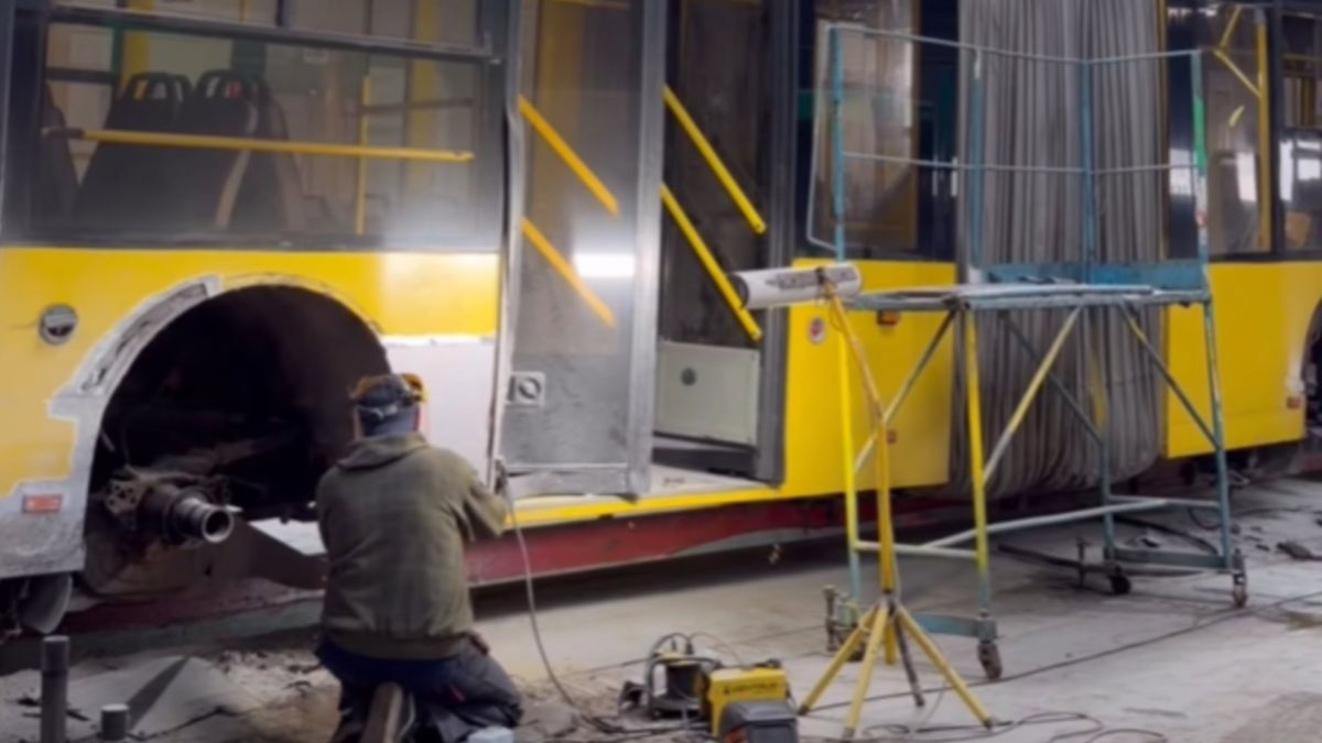 Працівник тролейбусного депо виконує ремонт кузова жовтого тролейбуса у ремонтній зоні