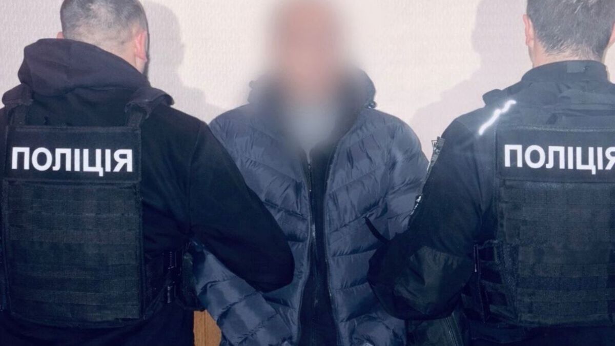 Двоє поліцейських у бронежилетах з написом ПОЛІЦІЯ конвоюють затриманого підозрюваного у продажу гранат та обрізу