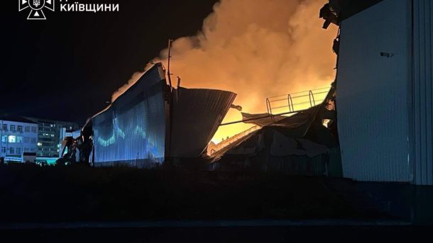 Зруйнована й охоплена вогнем покрівля складського ангару вночі, потужне полум'я освітлює навколишні будівлі