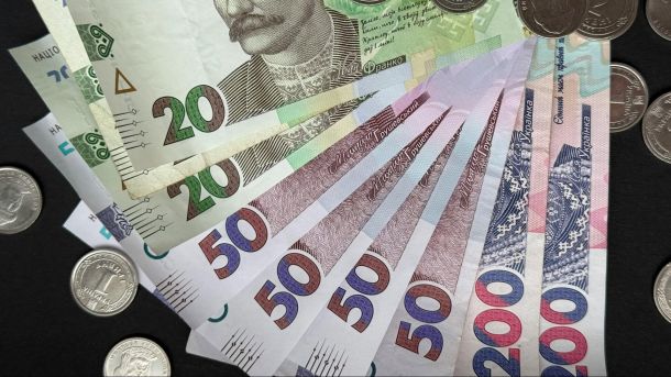 Українські гривні: банкноти номіналом 20, 50 та 200 гривень розкладені віялом поряд із монетами на темному фоні