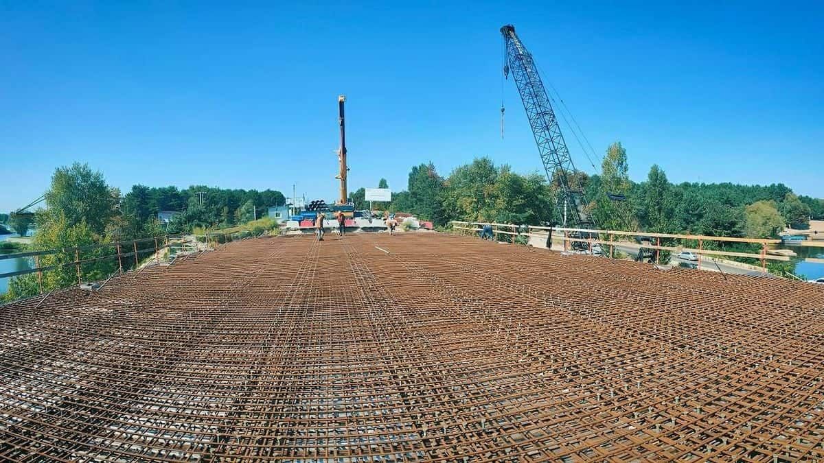будівництво мосту з арматурним каркасом, працює будівельна техніка та крани