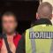 Поліцейський у жилеті з написом «Поліція» поруч із затриманим чоловіком у червоній куртці біля дверей квартири в Києві