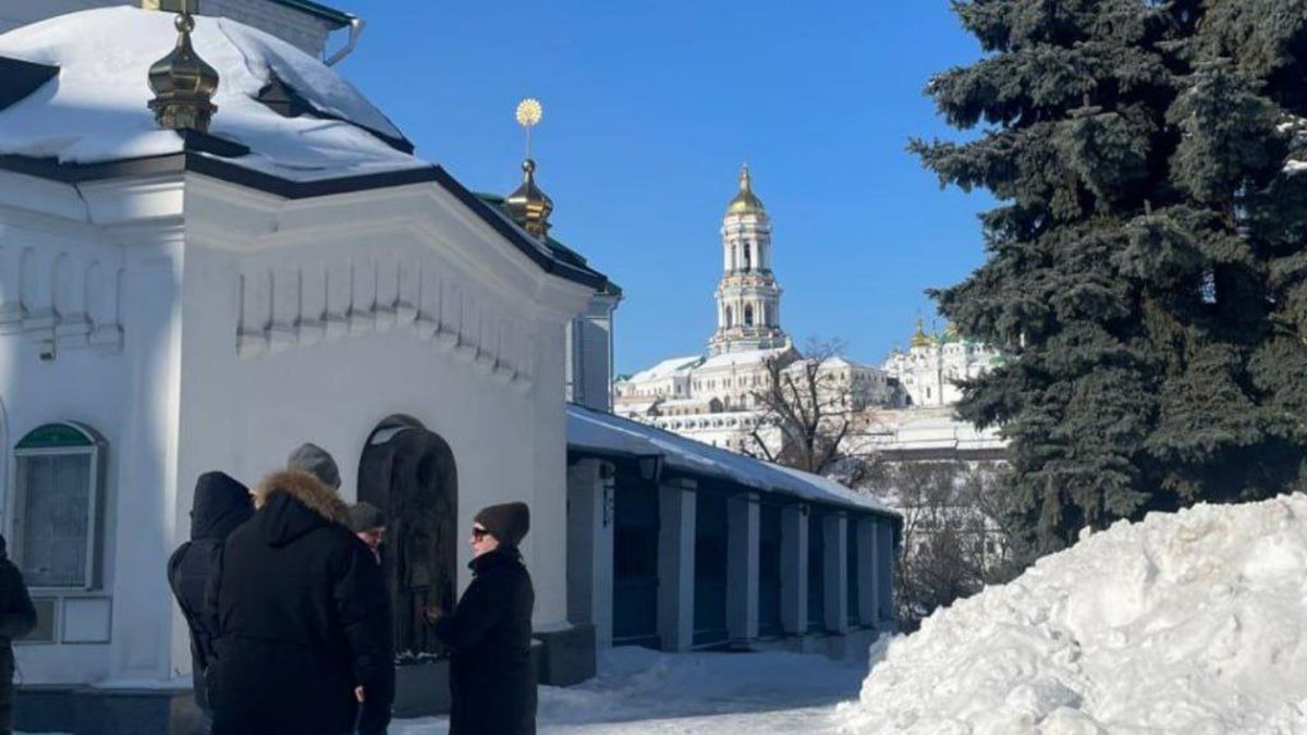 Люди стоять біля білої будівлі з арками на території Києво-Печерської Лаври взимку під час візиту місії ЮНЕСКО