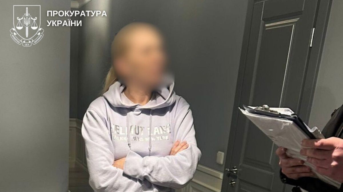 Жінка у світлому худі зі схрещеними руками, її обличчя розмите