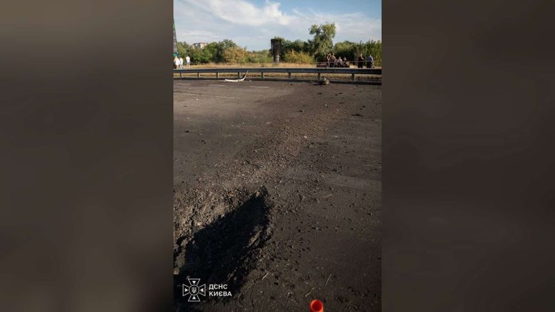 Обгоріла ділянка асфальту на проїзній частині, огороджена сигнальною стрічкою, на фоні — люди й дерева