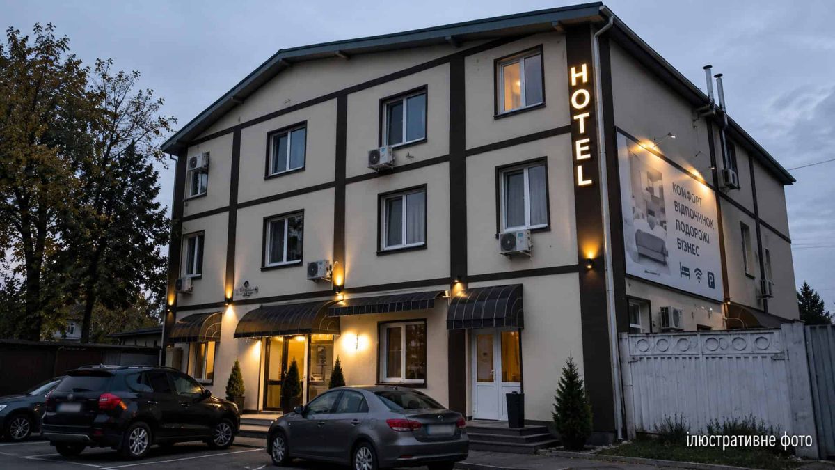 Ілюстративне фото: триповерхова будівля готелю з вивіскою HOTEL, освітленим фасадом і автомобілями на парковці у сутінках