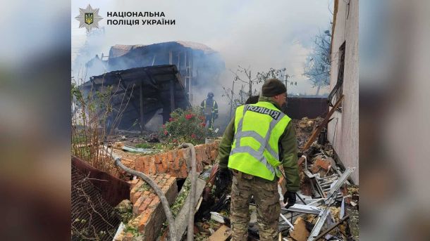 Поліцейський на місці пожежі приватного будинку після атаки безпілотників на Київ, на тлі рятувальник ДСНС і зруйновані споруди