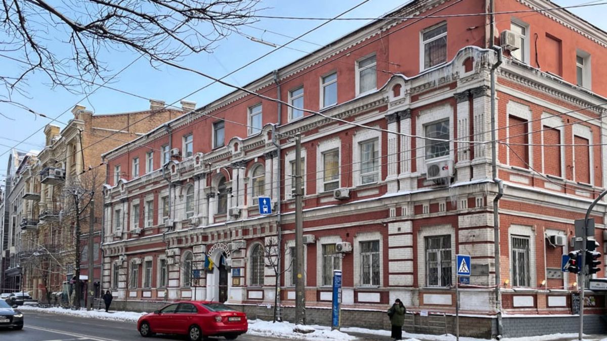 Триповерхова будівля початку ХХ століття з червоної цегли у центрі Києва взимку, з прапором України біля входу