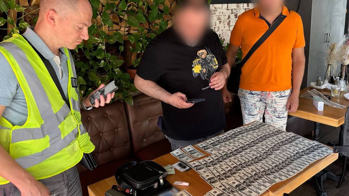 Поліцейський у жовтому жилеті фіксує вилучені долари на столі під час затримання підозрюваних у схемі фіктивного бронювання