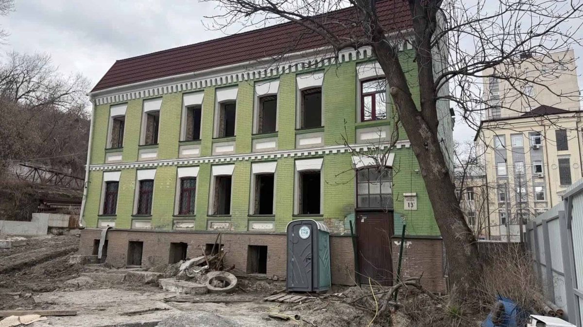 Двоповерховий зелений флігель Садиби Носача 1899 р. на вулиці Кирилівській, 13г у Києві — будівля оточена будівельним майданчиком, земля розрита, сміття навколо