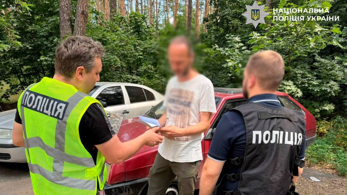 Два працівники поліції вручають підозру чоловіку в білій футболці із заблюреним обличчяч