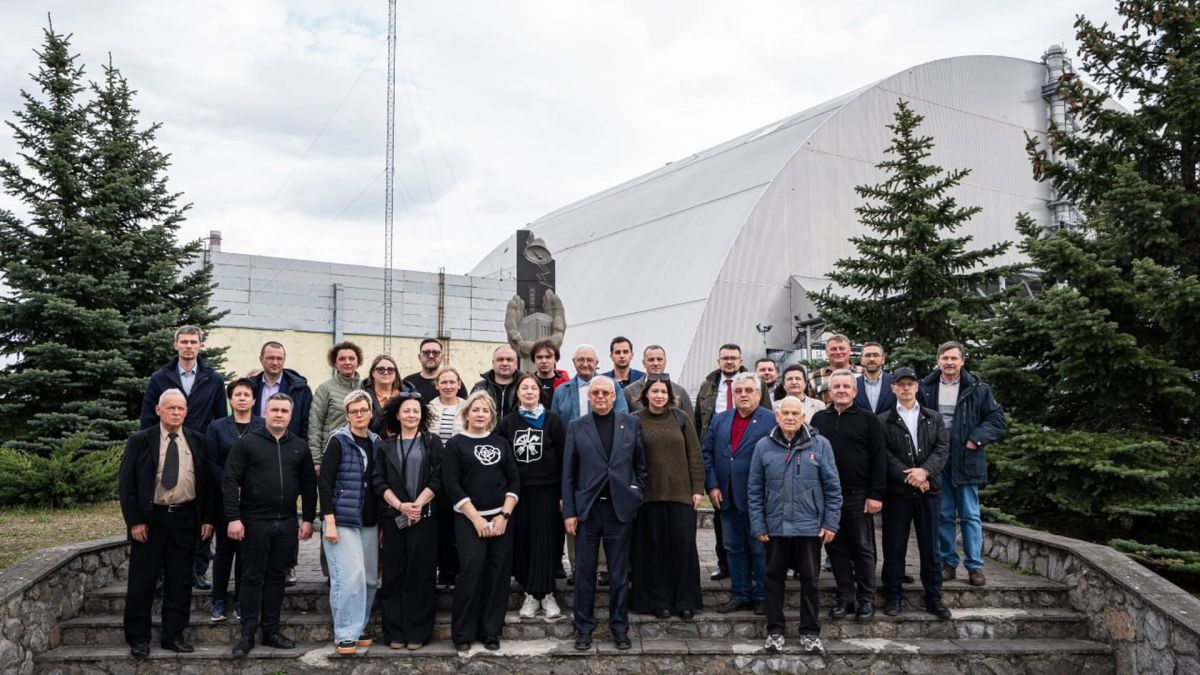 Учасники слухань Комітету Верховної Ради з питань соціальної політики у зоні відчуження на фоні арки Нового безпечного конфайнмента над четвертим блоком Чорнобильської АЕС