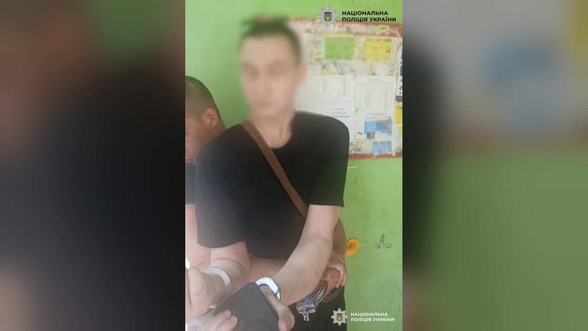 До суду скерували справу 21-річного киянина за ножове поранення однолітка Чоловік у кайданках із розмитим обличчям і поліцейський поруч на тлі зеленої стіни з оголошеннями, логотип Національної поліції України