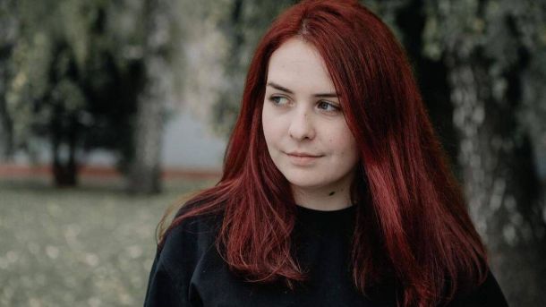 Красуня з яскравим русявим волоссям, що мило посміхається на природі у парку, оточена деревами і зеленню.