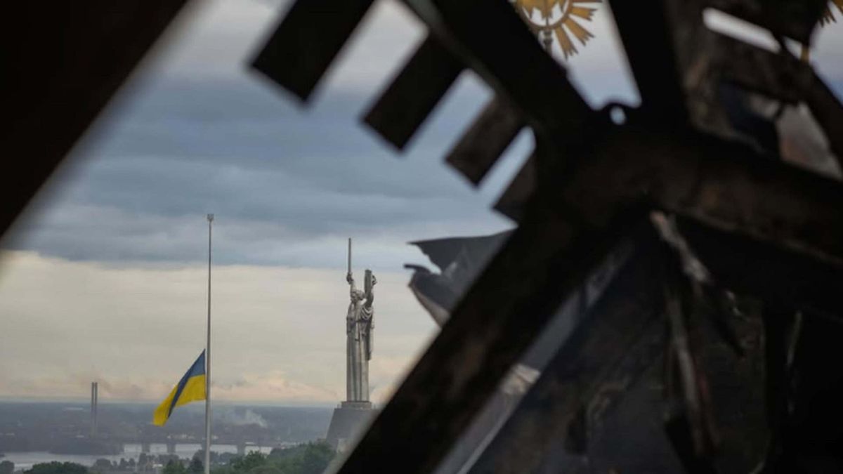 Монумент Батьківщина-Мати і приспущений прапор України крізь обгорілу конструкцію будівлі після обстрілу