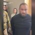 Затриманий чоловік із розмитим обличчям і правоохоронець у камуфляжі під час затримання у справі про напад із кислотою