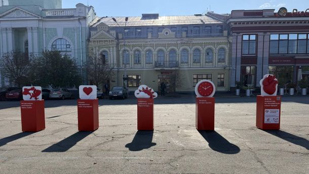 Червоні тумби з символами: карта тривог, лайк, погода, годинник і серце — інсталяція на Контрактовій площі у Києві