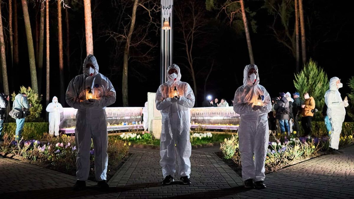 Учасники у захисних костюмах тримають свічки пам'яті біля меморіалу ліквідаторів Чорнобиля у Славутичі вночі на 26 квітня 2026 року