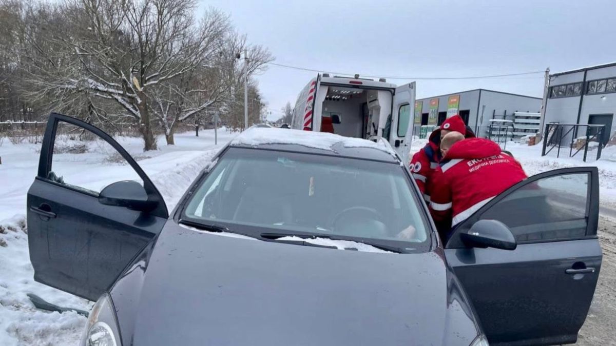 Парамедик екстреної медичної допомоги надає допомогу непритомній жінці в автомобілі з відкритими дверцятами на засніженій дорозі у Білій Церкві