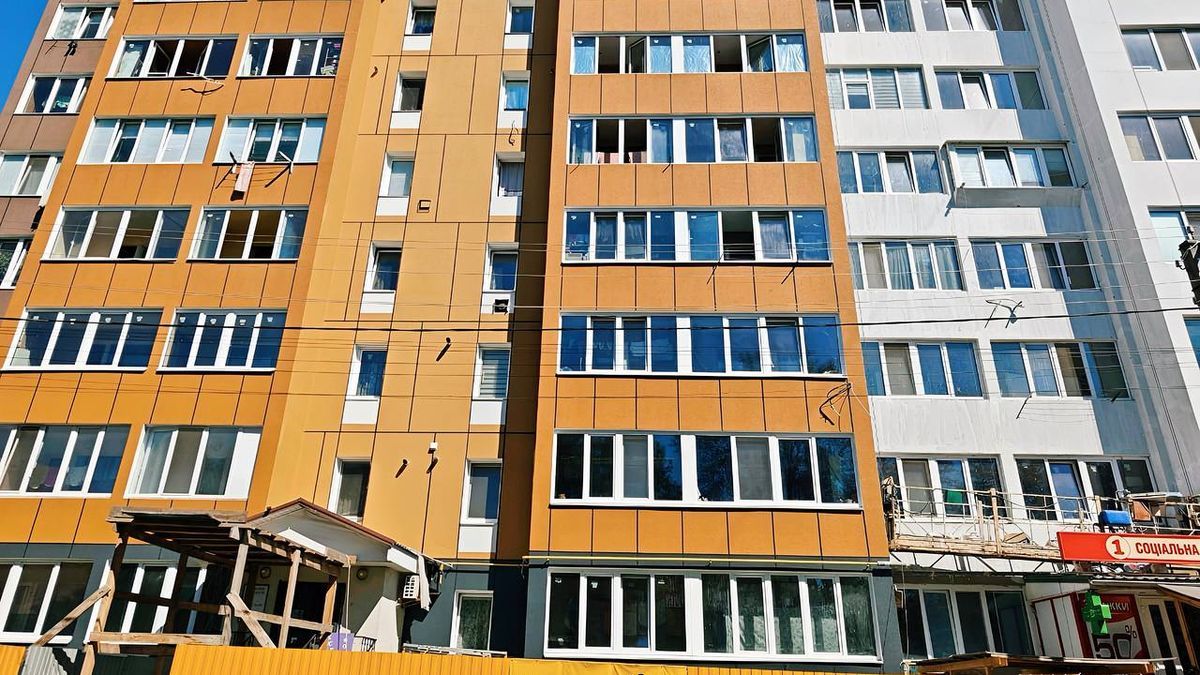 Вигляд сучасної жилої багатоповерхівки в Києві з яскраво оранжевими та білими фасадами, новобудова та ремонтні роботи у дворі, місто активно розвивається.