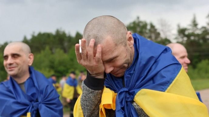 Чоловік, загорнутий у прапор України, емоційно прикриває обличчя рукою