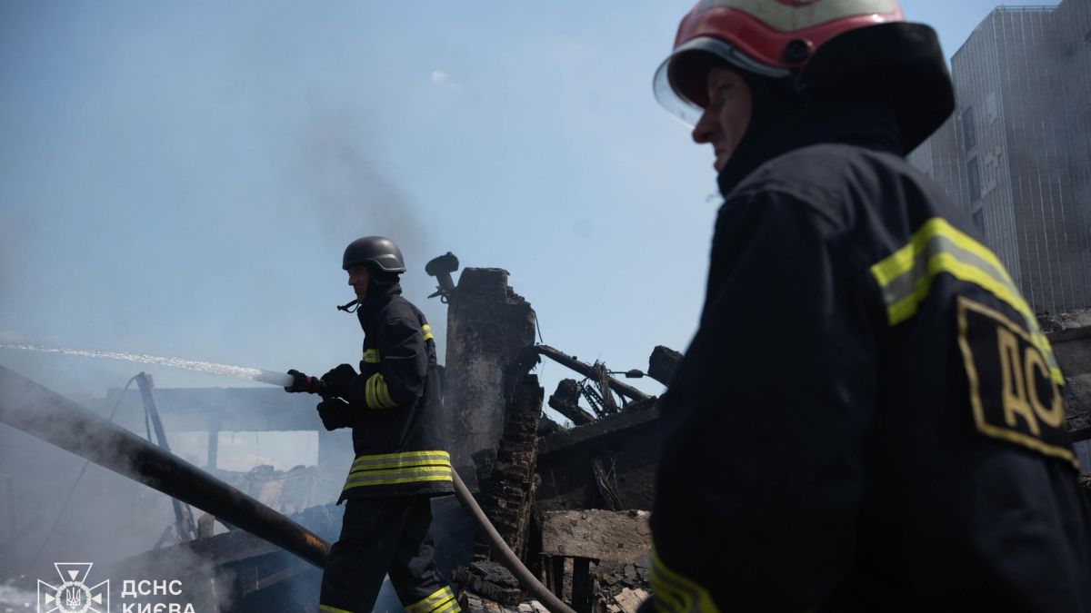 Рятувальники ДСНС Києва в захисних касках гасять пожежу з рукава серед обвуглених руїн зруйнованої будівлі після ракетно-дронової атаки на Дарницький район Києва
