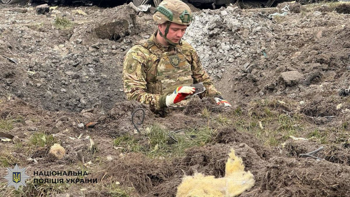 Вибухотехнік Національної поліції України працює у великій воронці від вибуху біля знищеного автомобіля Mercedes-Benz на проспекті Степана Бандери в Києві, 16 квітня 2026