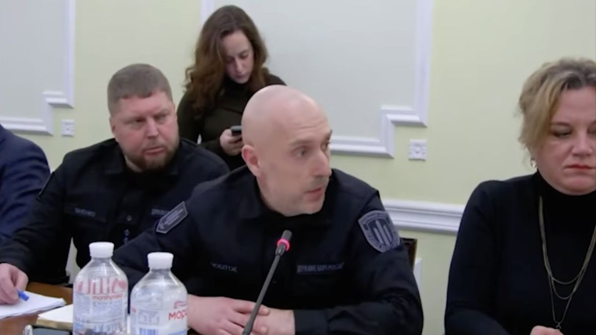Детективи ДБР сидять за столом і доповідають в мікрофон