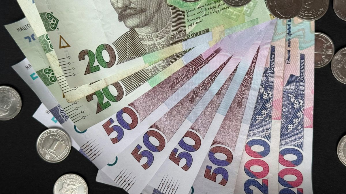 Українські гривні: банкноти номіналом 20, 50 та 200 гривень розкладені віялом поряд із монетами на темному фоні