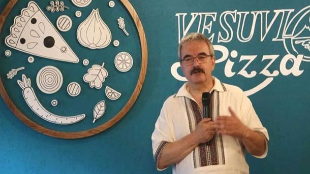 Мирон Спольський стоїть з мікрофоном біля стіни з намальованою піцою