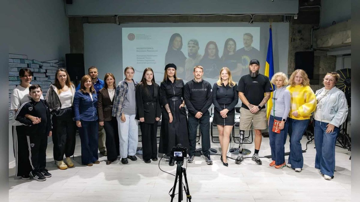 Група учасників зустрічі про інклюзію на тлі екрана зі слайдом, ветеран із протезом ноги, поруч прапор України