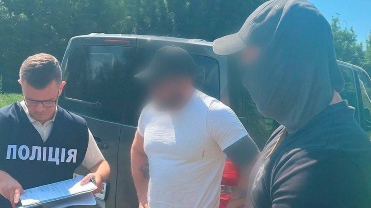 Поліцейський у жилеті «Поліція» зачитує документи підозрюваному у білій футболці біля автомобіля