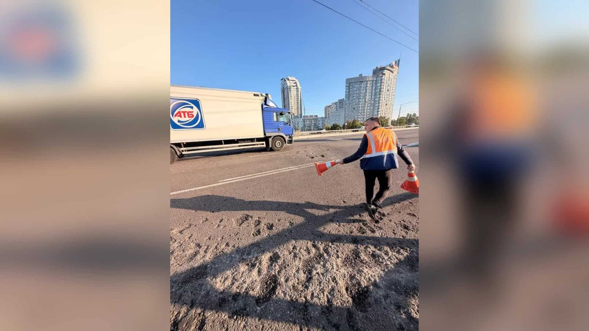 Дорожній працівник у сигнальному жилеті розставляє конуси на пошкодженому асфальті шляхопроводу проспекту Бандери в Оболонському р-ні Києва