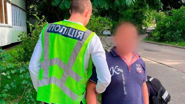 Працівник поліції тримає під руку чоловіка у дворі київської багатоповерхівки, обличчя заблюрене