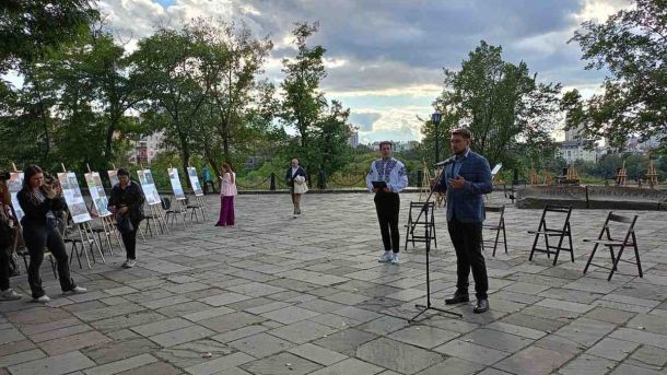 Вулична виставка на відкритому майданчику: чоловік у піджаку виступає біля мікрофона, поруч ведучий у вишиванці,