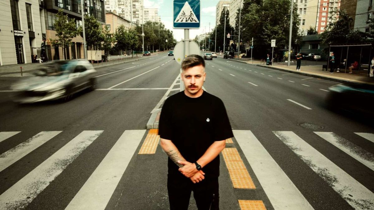 DJ Grim у чорному одязі стоїть на пішохідному переході на широкій вулиці Києва, презентуючи альбом «НЕ35ОРИМІ»