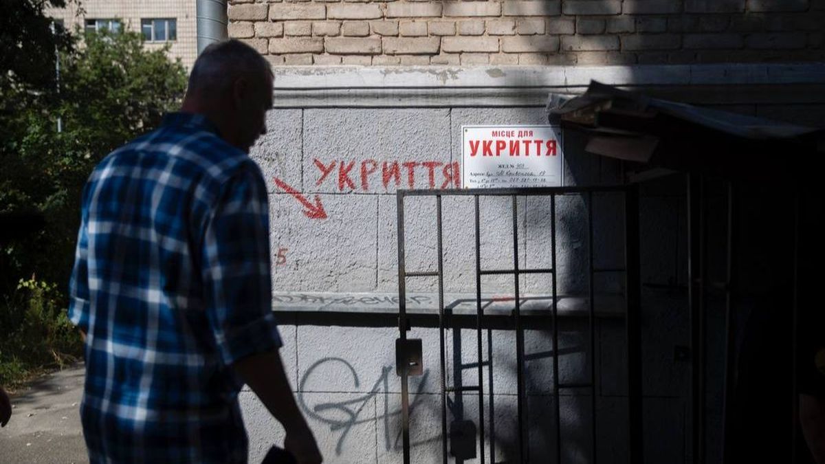 Відключене житло у Києві з табличкою "Місце для укриття" на стіні, з обличчям чоловіка, який проходить повз у місті під час повітряної тривоги.