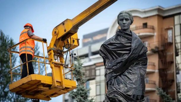 Комунальник у люльці автопідйомника знімає захисну плівку з пам'ятника Лесі Українці в Києві