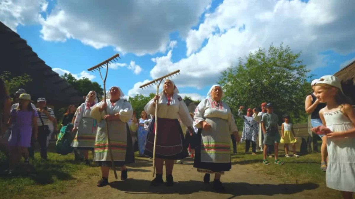 Жінки у народних костюмах з граблями йдуть дорогою музею просто неба під час фестивалю в Пирогові