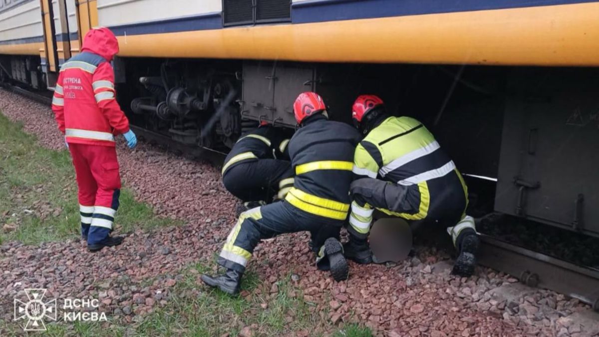 Рятувальники ДСНС у червоних касках деблокують тіло чоловіка з-під вагона приміського потяга на коліях у Святошинському районі Києва